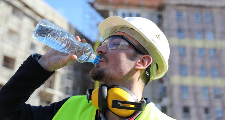 Worker At Construction Site With Bottle Of Water In The Summer